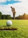 golf player putting golf ball into hole with sunshine
