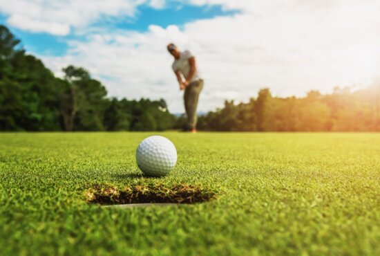 golf player putting golf ball into hole with sunshine